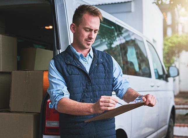 Person holding clipboard with van full of boxes in the background - link to The General Labs Business Insurance page