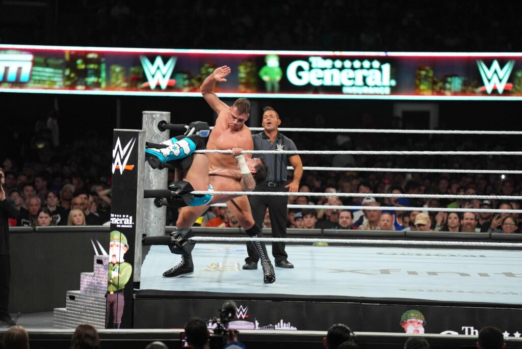WWE SummerSlam match action in the ring with The General Auto Insurance branding, promoting a VIP WWE experience sweepstakes.